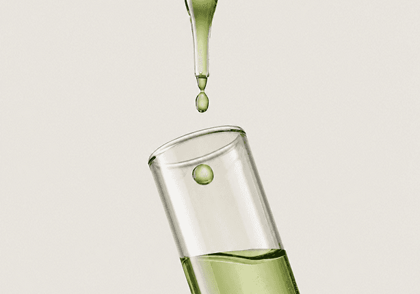 Gota verde cayendo sobre un tubo de ensayo con liquido vegetal.
